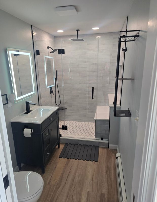 Remodeled bathroom with tiled walk-in glass shower, navy vanity, lighted mirror and wood-look floor