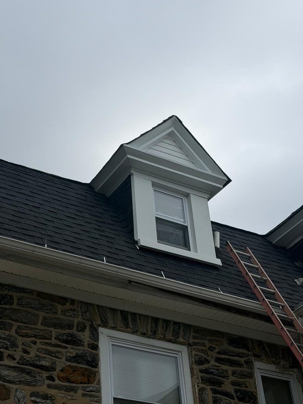 Angled view of a new dormer with white trim and new shingle roof on a stone house
