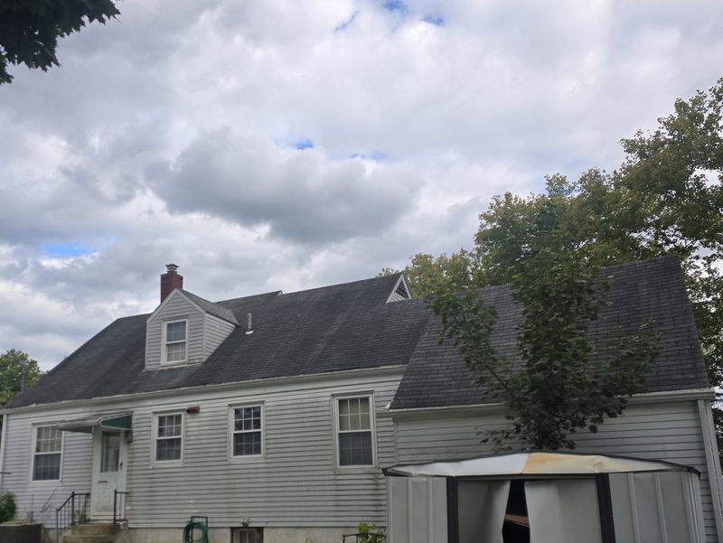 Cape Cod house before roof replacement: old, dark, weathered shingles on the main roof, dormer and side section