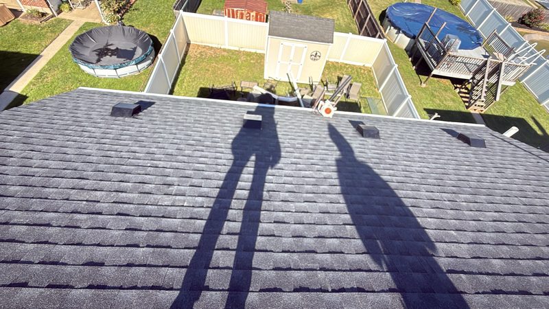 View down a newly shingled roof with dark gray architectural shingles and roof vents